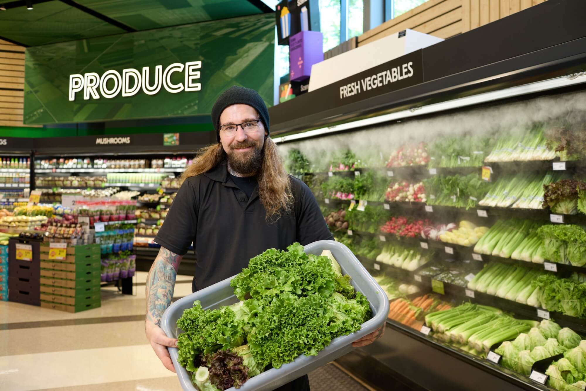 Employé de Sobeys tenant un bac de laitue devant un mur mouillé