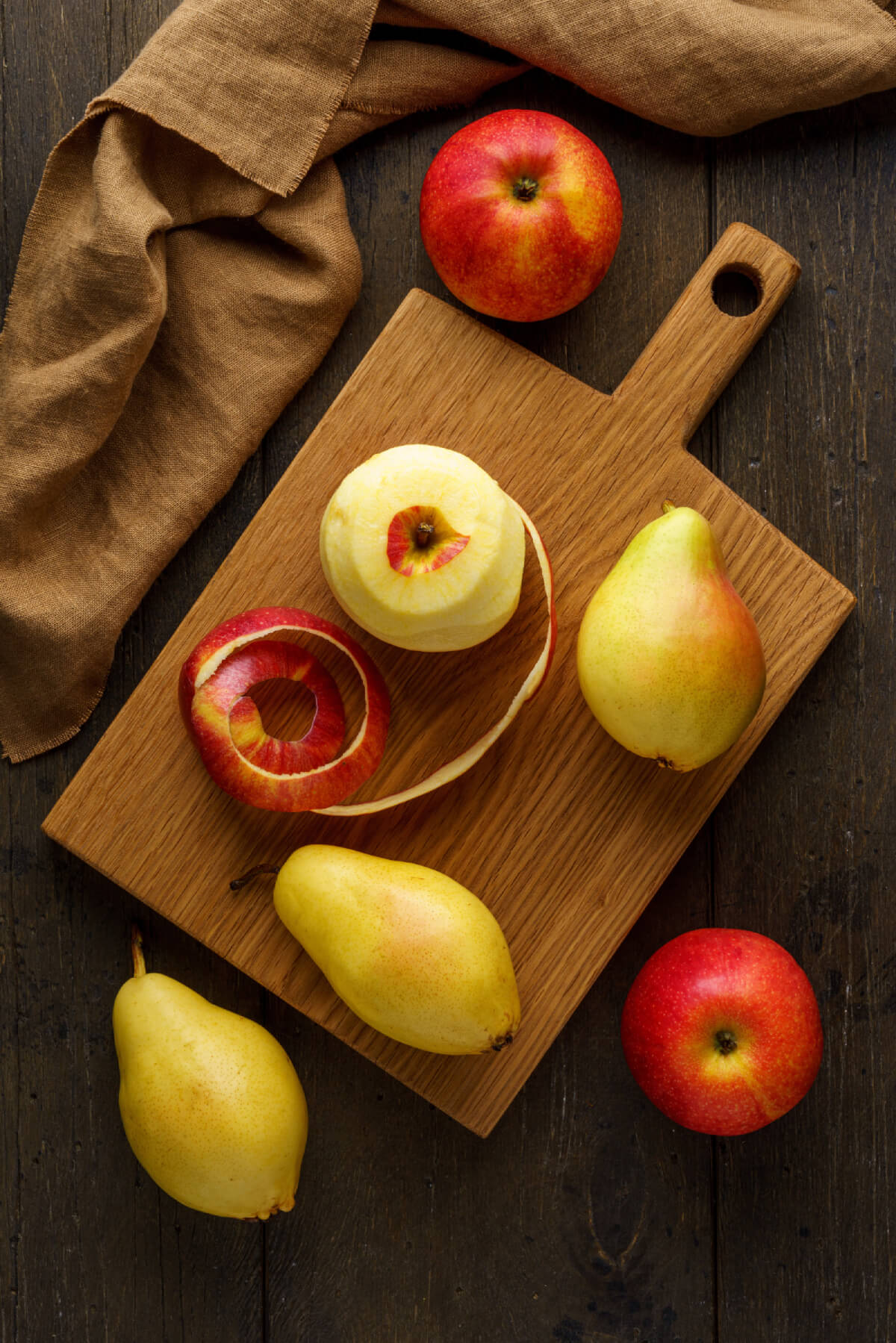 Pommes et poires sur une planche à découper avec une pomme presque entièrement pelée, avec la pelure à côté